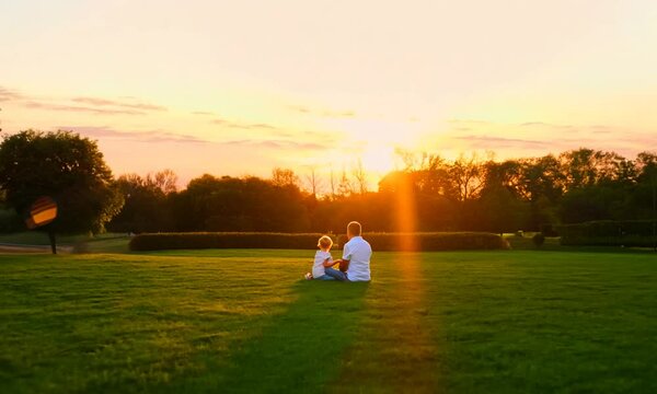 Father and Child Sitting in Park at Sunset 