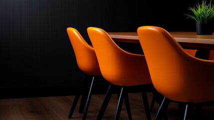 Three orange chairs sit around a wooden table against a dark background.  A small plant sits on the table.