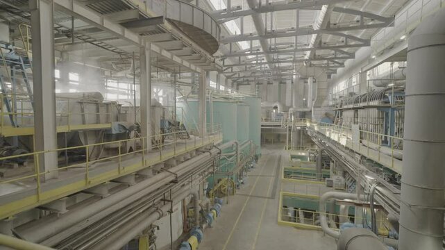 Large hall of cardboard factory with machinery pipes and tanks. Equipment serves as production resource for creation of finished material