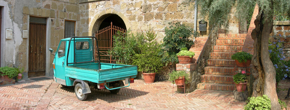 A classic 1959  Piaggio APE, a  3 wheeled vehicle scooter truck, in a courtyard in Tuscany Italy .The Piaggio Ape (Italian for bee ) was   initially marketed as a TriVespa commercial vehicle . 