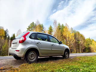 Silver car parked on a scenic road surrounded by autumn foliage and a clear blue sky