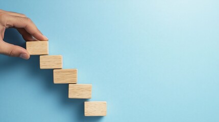 A hand placing wooden blocks in a staircase formation on a blue background.