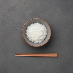 A Top-Down View of a Bowl Filled with Steamed White Rice on a Gray Surface Accompanied by Wooden Chopsticks for Culinary Imagery