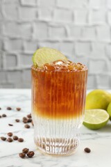 Refreshing espresso tonic drink with slice of lime and coffee beans on white marble table