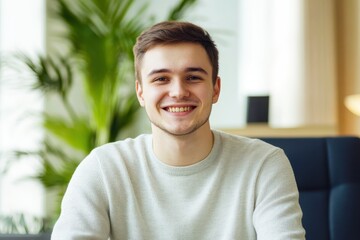 Cheerful young man smiling brightly while sitting in a modern office with greenery, showcasing a positive and relaxed atmosphere, ideal for commercial use