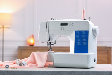 Sewing machine with threads, measuring tape and fabric on white table in workshop