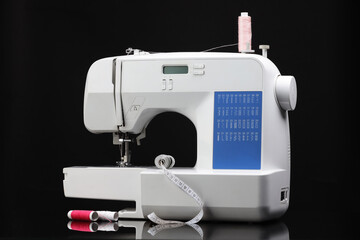 Sewing machine with measuring tape and spools of threads on black background