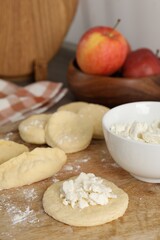 Making pirozhki (stuffed pastry pies). Pieces of dough with cottage cheese on wooden table, closeup