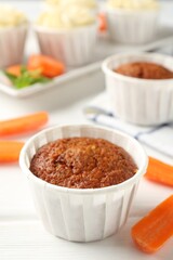 Delicious carrot muffins and fresh vegetables on white wooden table, closeup