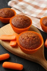 Delicious carrot muffins with fresh vegetables on black table, closeup