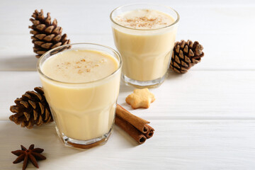 Tasty Christmas cocktail (eggnog) in glasses, pine cones and spices on white wooden table, closeup. Space for text