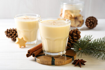 Tasty Christmas cocktail (eggnog) in glasses, pine cones and spices on white wooden table, closeup