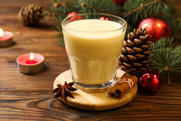Tasty Christmas cocktail (eggnog) in glass, festive decor and burning candles on wooden table, closeup
