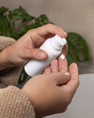 Woman in brown bathrobe pumping cream on finger and holding a cosmetic bottle in bathroom