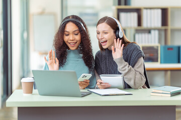 Two female students work together in a coffee shop, chatting and discussing projects. With a laptop, searching for information on the internet