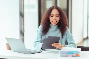 Beautiful African girl sitting at the table Looking at the laptop screen, he looks happy reading an email message with good news. Chat with customers online