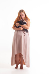 A girl in a dress and a cat posing in the studio. Beautiful young pregnant woman in dress posing on white background