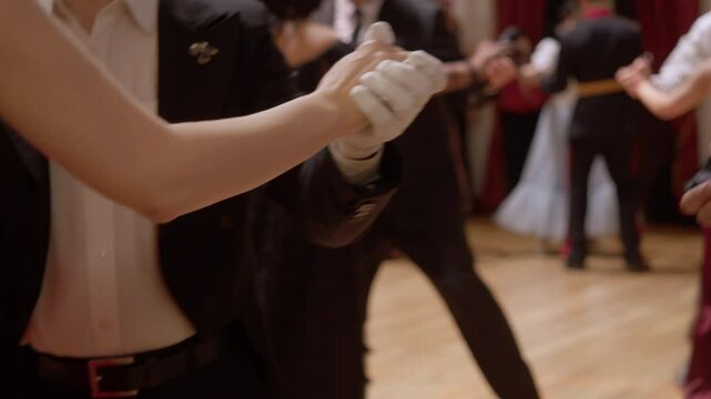 Several young couples are dancing in elegant costumes, dresses and gloves. They are cosplaying old dances from the 19th century.