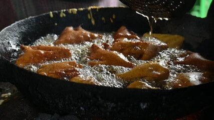 Bread pakora is being fried in hot oil. It is made by stuffing the bread with potatoes and dipping it in the batter of chickpea flour and then frying it. popular snack of India. Slow motion video. 