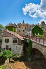 Titel: View at the medieval village of Carennac in Lot Occitanie Southern France with bridge under a blue sky with clouds in summer