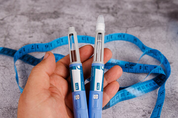 Hand with semaglutide pens and measuring tape on cement surface