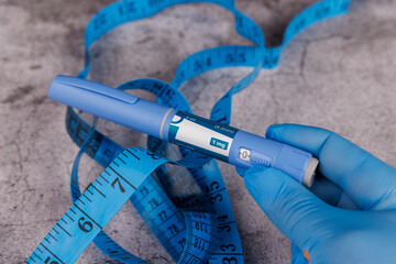 Blue-gloved hand holding semaglutide medication pens and measuring tape.
