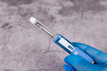 Gloved hand with diabetes pens and measuring tape on cement background.