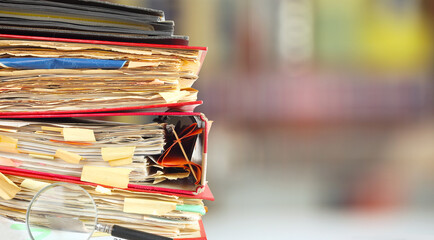 stack of messy file folders, blurred bookshelf in the back,red tape, bureaucracy,beat the clock...