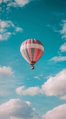 Naklejka premium Pink and teal hot air balloon soaring in a vibrant blue sky with fluffy white clouds.