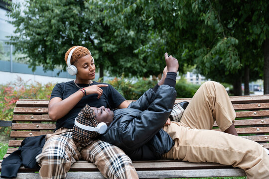 Relaxed multiethnic LGBT couple listening to music on a bench in the park