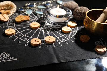 Wooden runes and burning candle on divination mat, closeup