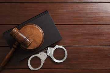 Handcuffs, judge's gavel and book on wooden table, flat lay. Space for text