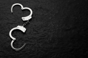 Metal chain handcuffs on black table, top view. Space for text