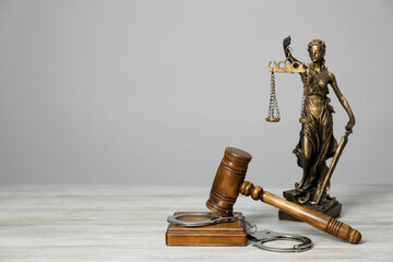 Handcuffs, judge's gavel and Lady Justice figure on white wooden table, space for text