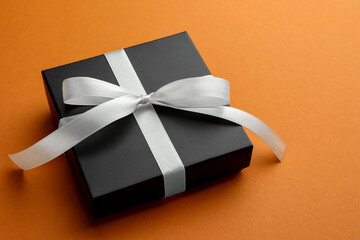 Beautiful gift box with bow on orange background, closeup