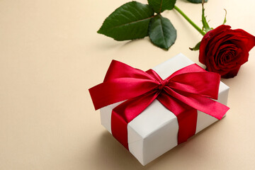 Beautiful gift box with red bow and rose on beige background, closeup. Space for text