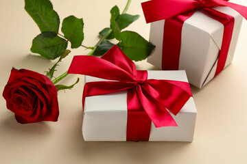 Beautiful gift boxes with red bows and rose on beige background, closeup