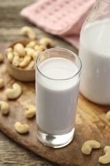 Fresh cashew milk in glass and nuts on wooden table, closeup