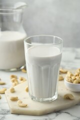 Fresh cashew milk in glass and nuts on white marble table against light background, closeup