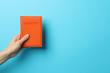 Woman holding passport in bright cover on light blue background, closeup. Space for text