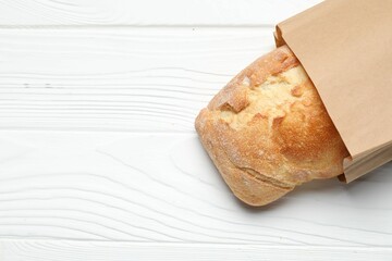 Paper bag with fresh baguette on white wooden table, top view. Space for text