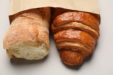 Paper bag with fresh baguette and croissant on light gray table, closeup