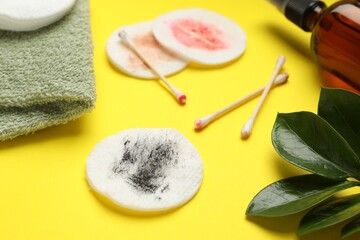 Dirty cotton pads, swabs, cosmetic product, towel and green leaves on yellow background, closeup