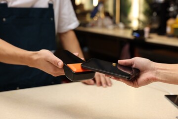 Woman paying with smartphone via terminal in cafe, closeup