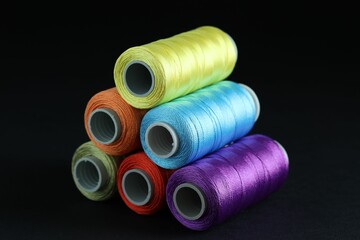 Spools of colorful sewing threads on black background, closeup