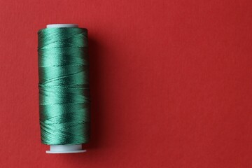 Spool of green sewing thread on red background, top view. Space for text