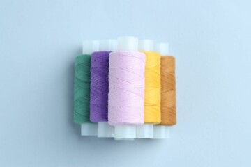 Spools of colorful sewing threads on light background, top view
