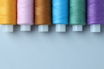 Spools of colorful sewing threads on light background, flat lay. Space for text