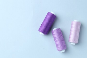 Spools of colorful sewing threads on light background, flat lay. Space for text