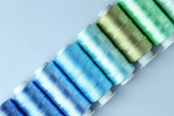 Spools of colorful sewing threads on light background, flat lay